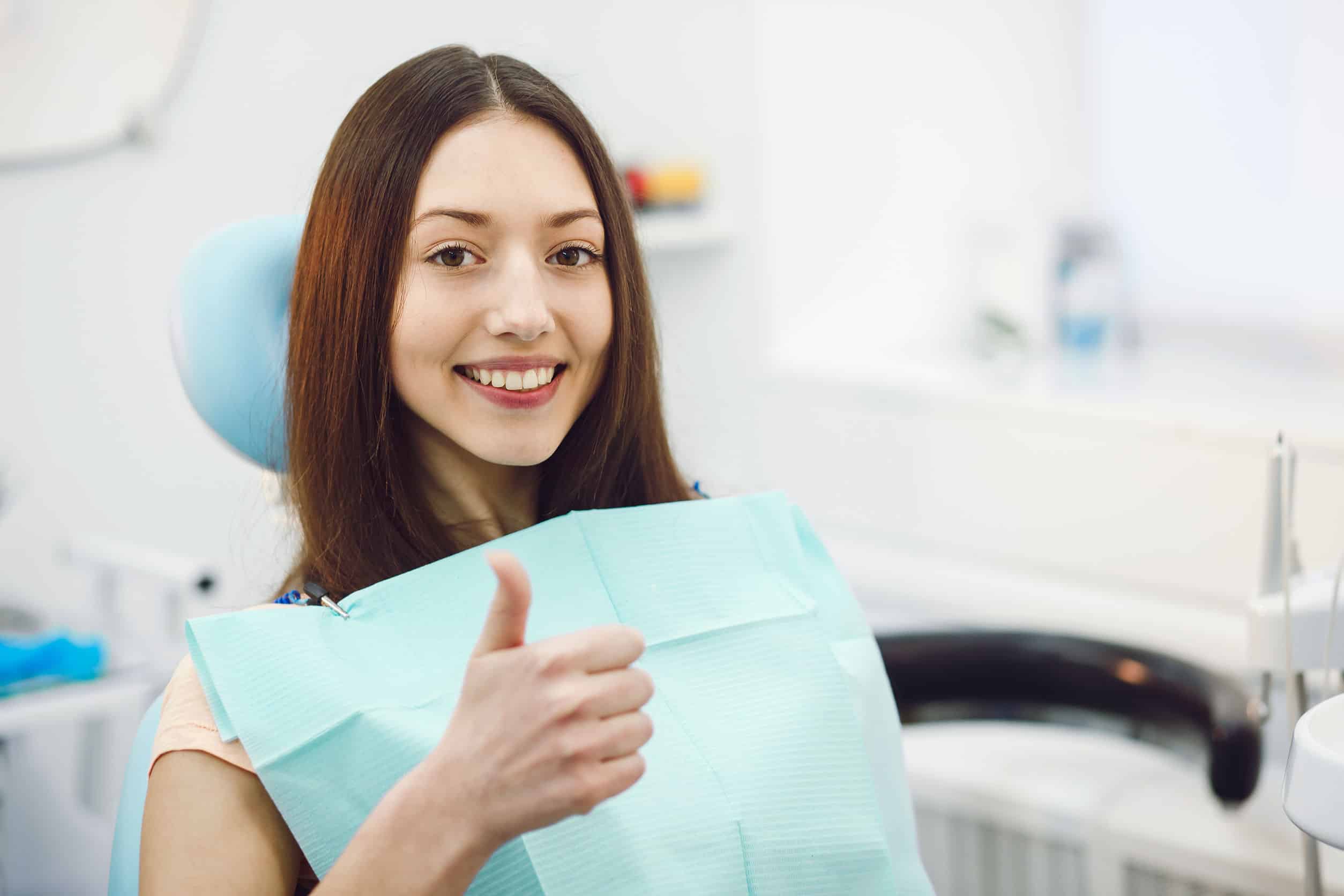 Smiling woman giving thumbs up in a dental clinic after treatment
