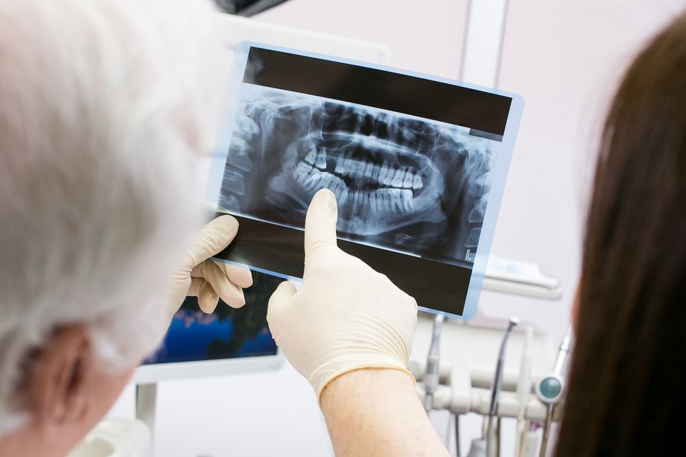 Dentist wearing gloves pointing at a dental X-ray image while discussing it with a patient