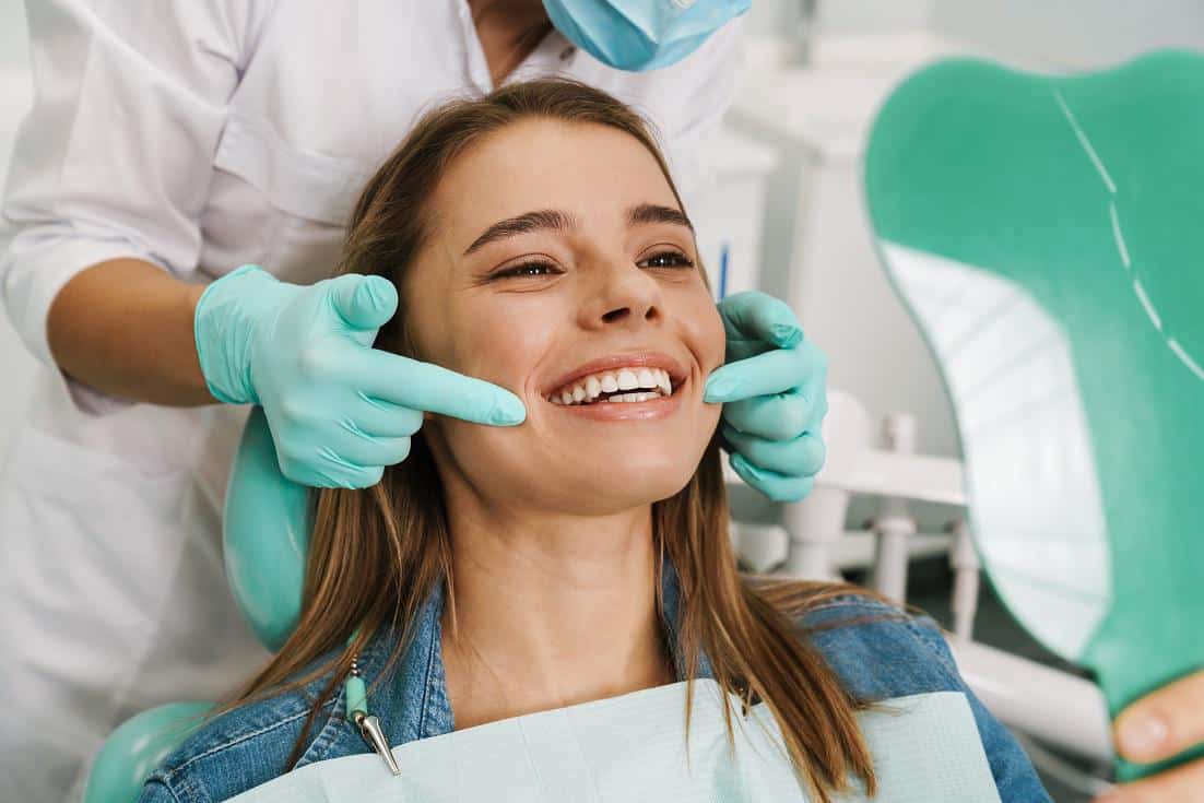 Dentist examining a smiling patient’s teeth during a dental restoration consultation in a dental clinic.
